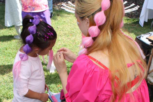 Woman styling a young girl's hair with colorful extensions outdoors.