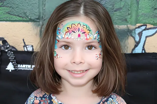 Young girl with colorful face painting and floral design.
