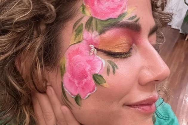 Floral face paint with pink roses and green leaves on woman's cheek.