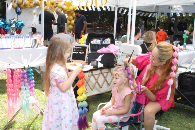 Woman styling girls' hair with colorful braids at outdoor event.