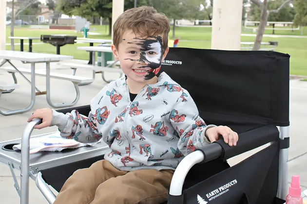 Child sitting on a chair with face painted in a park.