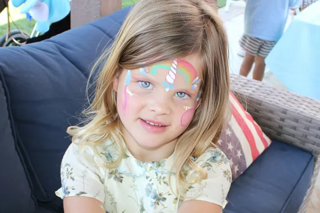 Young girl with colorful face paint sitting on a blue couch.