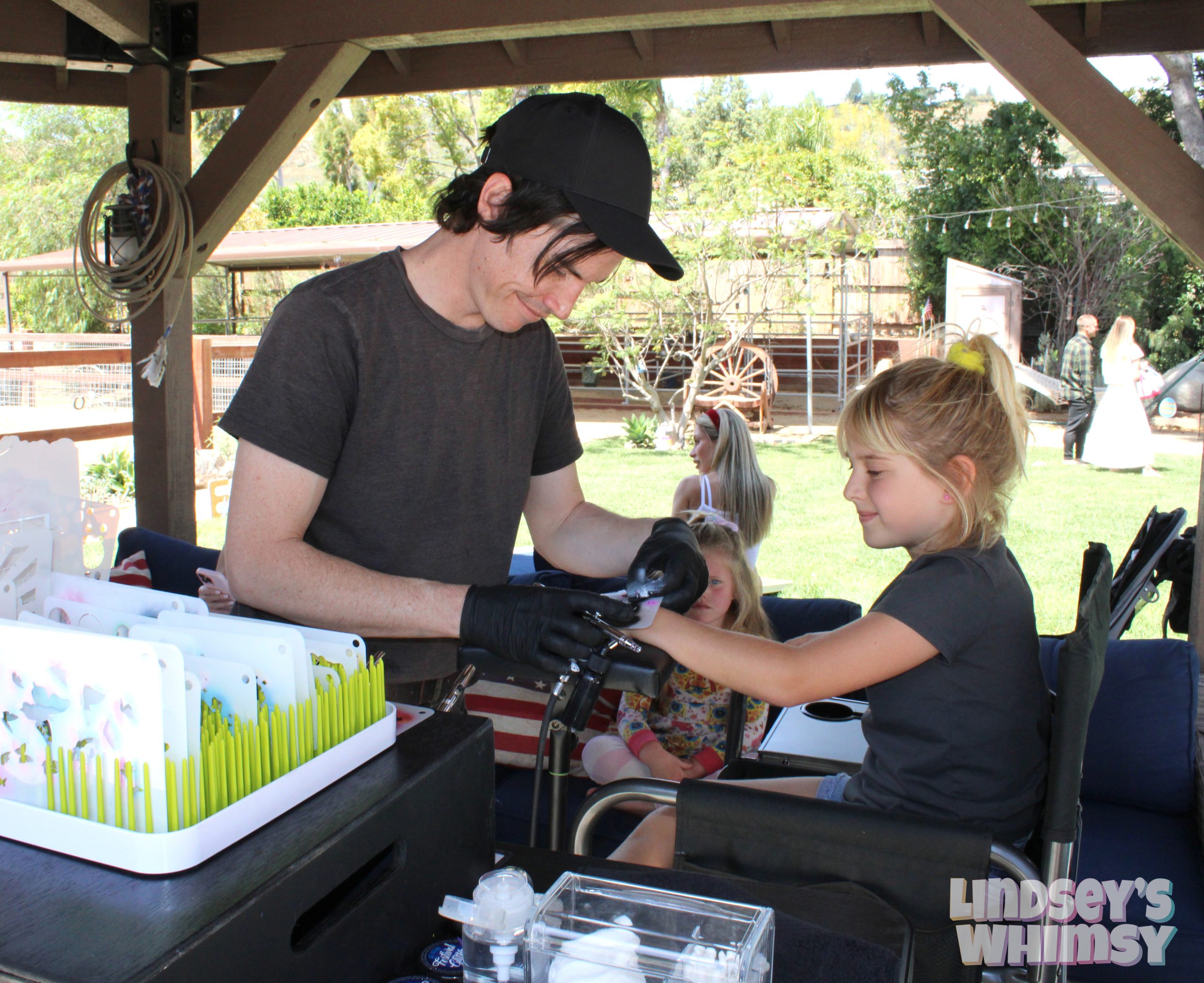 Man applying airbrush tattoo to a smiling child at outdoor event.