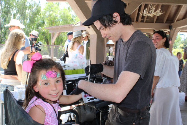 Artist applying airbrush tattoo on young girl at outdoor event.